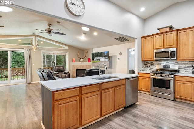 kitchen with appliances with stainless steel finishes, tasteful backsplash, vaulted ceiling, a kitchen island with sink, and sink