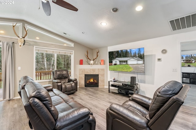 living room with light hardwood / wood-style floors, ceiling fan, lofted ceiling, and a tiled fireplace