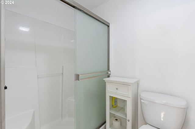 bathroom featuring a shower with door and toilet