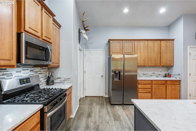 kitchen featuring decorative backsplash, stainless steel appliances, light stone countertops, and light hardwood / wood-style floors