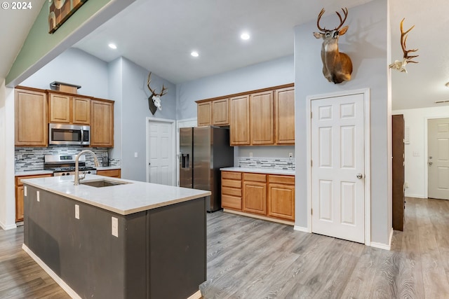 kitchen featuring sink, backsplash, an island with sink, light hardwood / wood-style floors, and appliances with stainless steel finishes