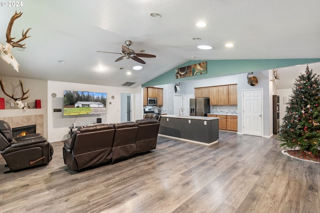 living room with hardwood / wood-style floors, lofted ceiling, sink, ceiling fan, and a tiled fireplace