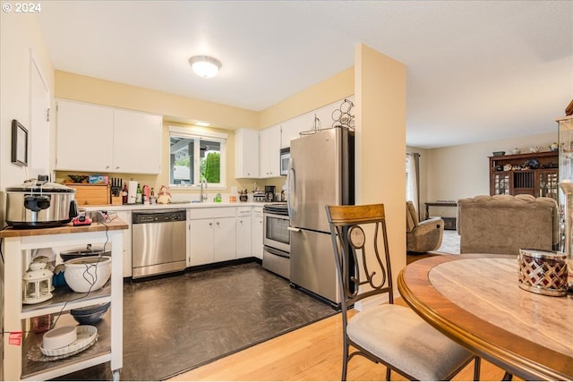 kitchen with stainless steel appliances, a sink, white cabinetry, open floor plan, and light countertops