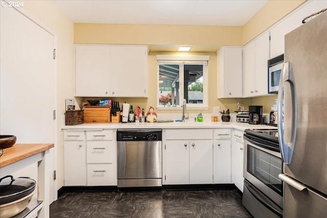 kitchen with stainless steel appliances, sink, white cabinetry, and dark tile patterned flooring