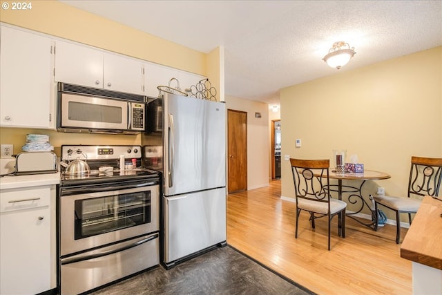 kitchen with a textured ceiling, wood finished floors, white cabinets, light countertops, and appliances with stainless steel finishes