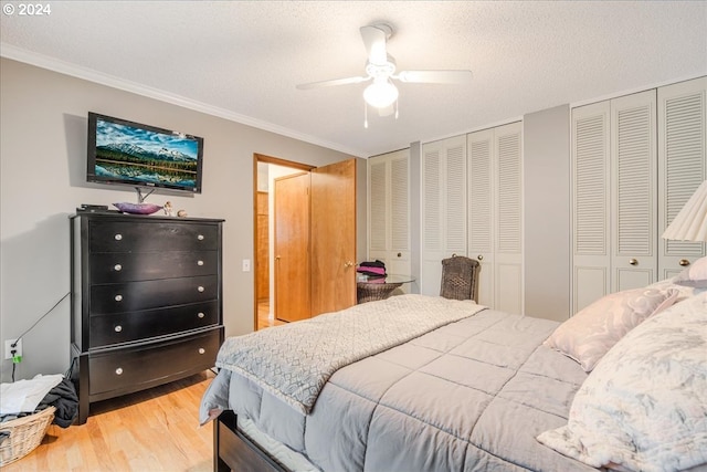 bedroom with a textured ceiling, ceiling fan, light wood-type flooring, and multiple closets