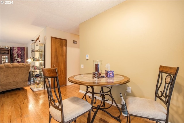 dining room featuring hardwood / wood-style flooring, a textured ceiling, and vaulted ceiling