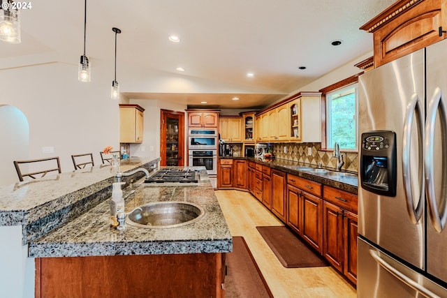 kitchen featuring sink, vaulted ceiling, stainless steel appliances, a breakfast bar area, and light hardwood / wood-style floors