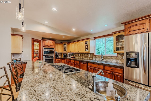 kitchen featuring stainless steel appliances, sink, pendant lighting, vaulted ceiling, and a kitchen breakfast bar