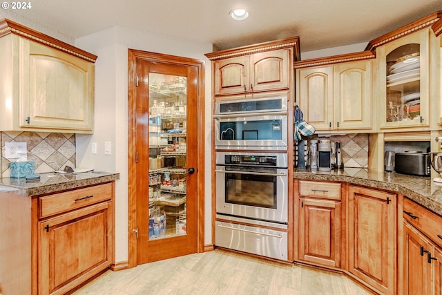 kitchen with tasteful backsplash, light brown cabinetry, light hardwood / wood-style floors, and double oven