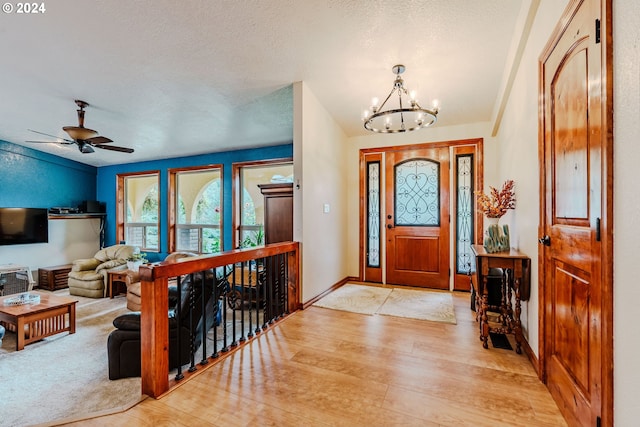 foyer entrance with ceiling fan with notable chandelier, light wood-type flooring, and a textured ceiling