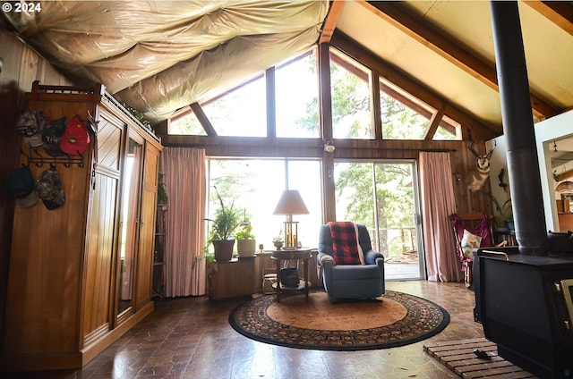 living area with high vaulted ceiling, a wood stove, wood walls, and stone finish flooring