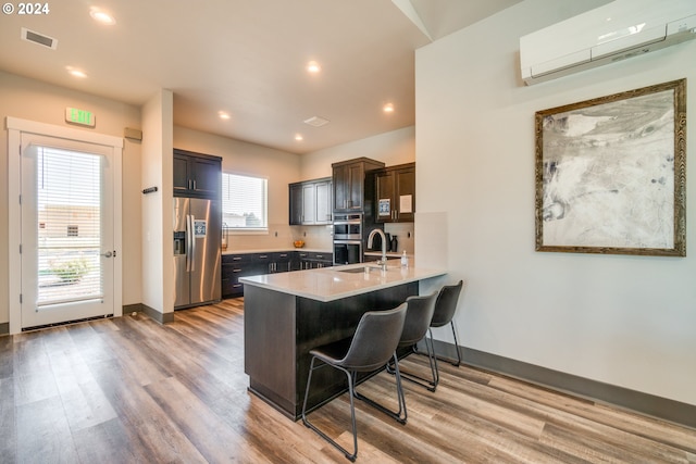 kitchen with kitchen peninsula, light wood-type flooring, a breakfast bar, stainless steel appliances, and an AC wall unit