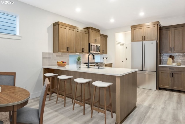 kitchen featuring a breakfast bar area, decorative backsplash, light wood-type flooring, kitchen peninsula, and stainless steel appliances