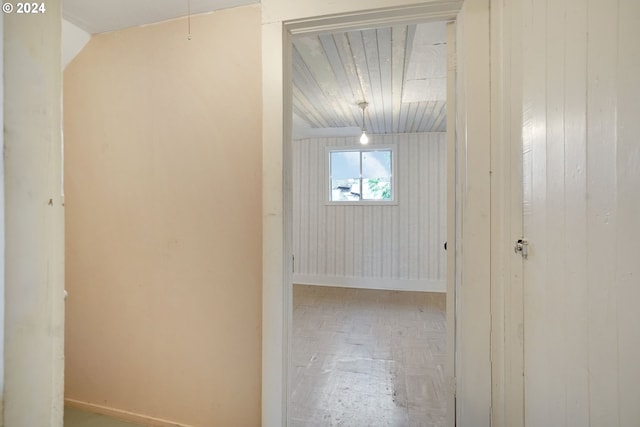 corridor with wooden walls, lofted ceiling, and parquet floors