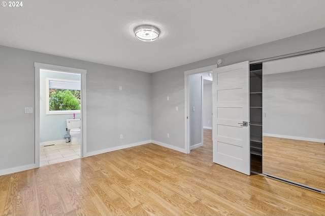 unfurnished bedroom featuring ensuite bathroom, light hardwood / wood-style floors, and a closet