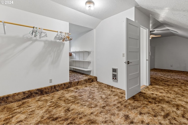 interior space with heating unit, vaulted ceiling, carpet flooring, and a textured ceiling