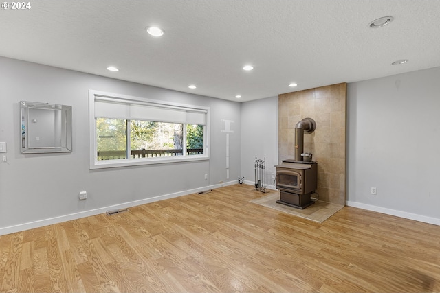 unfurnished living room featuring light hardwood / wood-style floors, a textured ceiling, and a wood stove