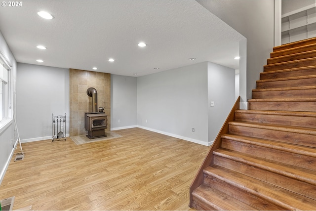 unfurnished living room with light wood-type flooring, a textured ceiling, and a wood stove