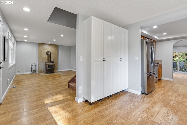 kitchen with light hardwood / wood-style floors, stainless steel refrigerator, white cabinetry, a textured ceiling, and a wood stove