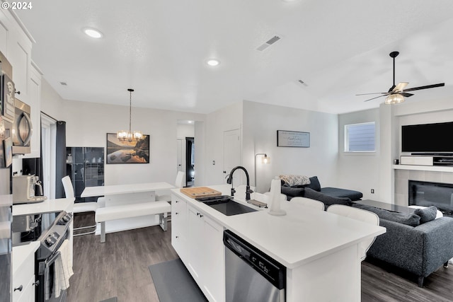 kitchen featuring appliances with stainless steel finishes, white cabinets, ceiling fan with notable chandelier, a center island with sink, and sink