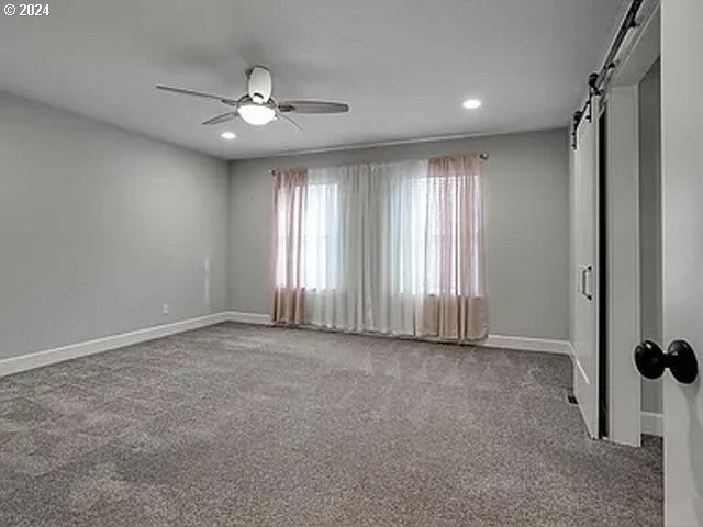 unfurnished bedroom with ceiling fan, carpet flooring, and a barn door