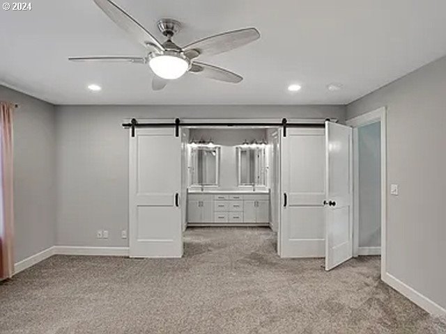 unfurnished bedroom with ceiling fan, light carpet, and a barn door