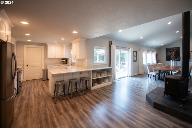 kitchen with sink, a wood stove, kitchen peninsula, stainless steel fridge, and white cabinetry