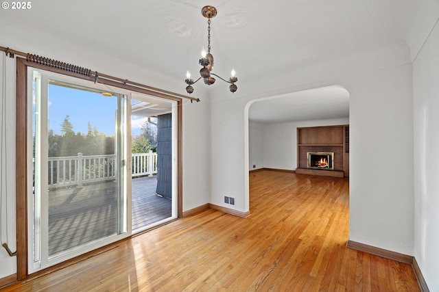 unfurnished dining area featuring a brick fireplace, a notable chandelier, and light hardwood / wood-style floors