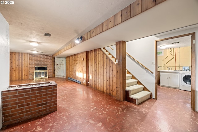 basement featuring washer / dryer, wood walls, a textured ceiling, baseboard heating, and a fireplace