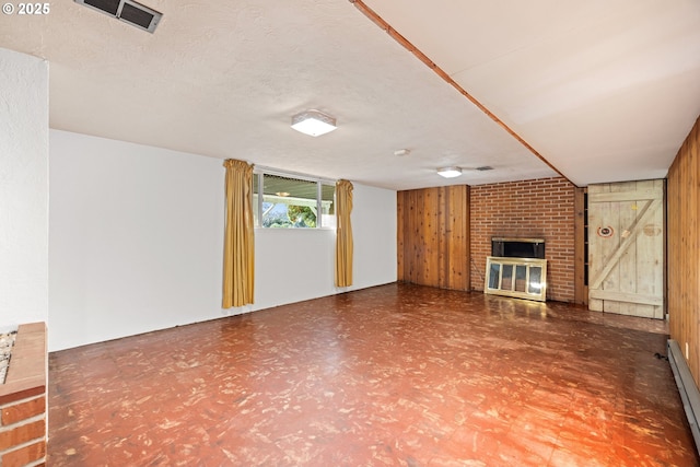 unfurnished living room with a brick fireplace, a baseboard heating unit, wooden walls, and a textured ceiling