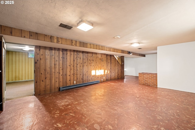 basement featuring wooden walls, a textured ceiling, and baseboard heating