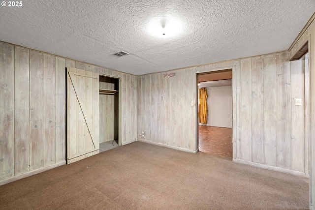 unfurnished bedroom with light carpet, a closet, a textured ceiling, and wood walls