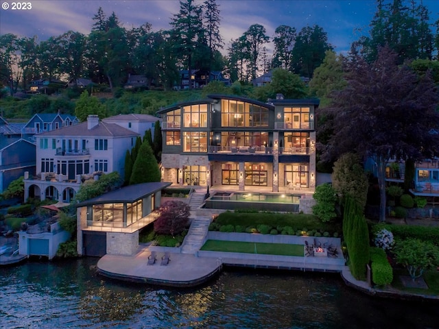 back house at dusk featuring a water view, a patio area, and a balcony