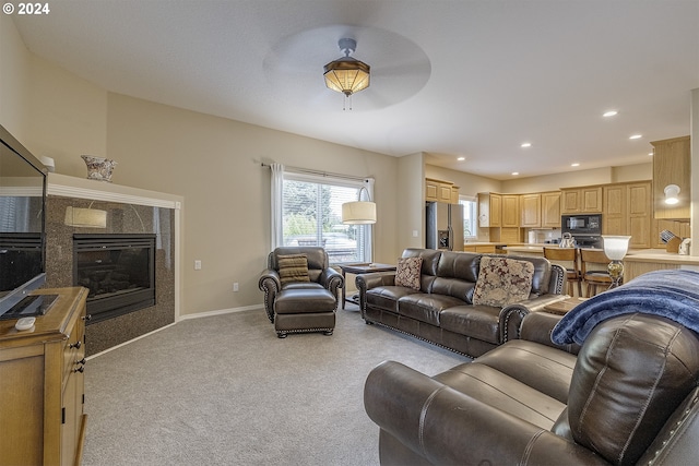 living room with ceiling fan, a tiled fireplace, and light carpet