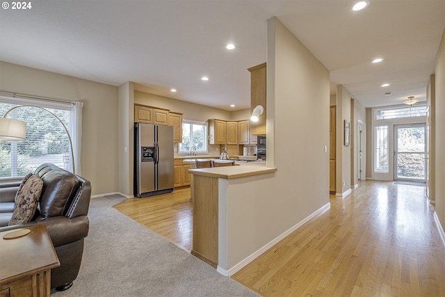 kitchen with light wood-type flooring, stainless steel refrigerator with ice dispenser, light brown cabinetry, sink, and kitchen peninsula