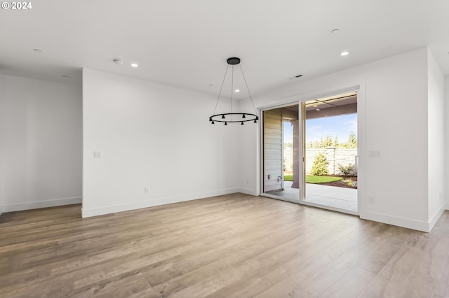 spare room with a notable chandelier and light hardwood / wood-style flooring