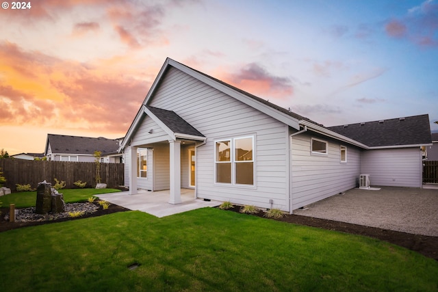 back house at dusk featuring a lawn, a patio area, and central AC