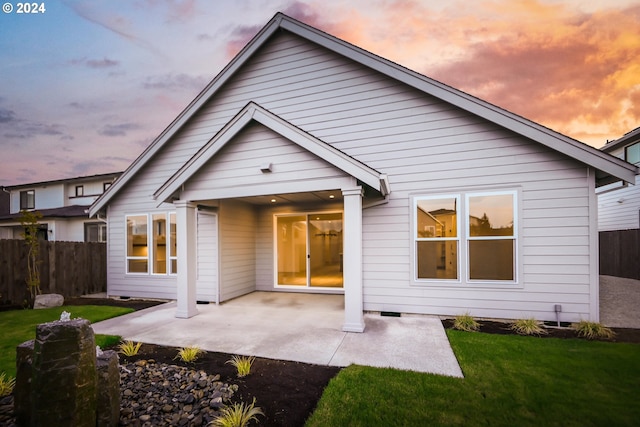 back house at dusk with a patio and a lawn