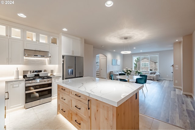 kitchen featuring a center island, white cabinets, hanging light fixtures, range hood, and stainless steel appliances