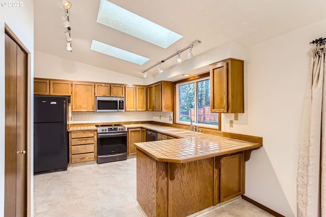 kitchen with sink, tile countertops, kitchen peninsula, vaulted ceiling with skylight, and appliances with stainless steel finishes