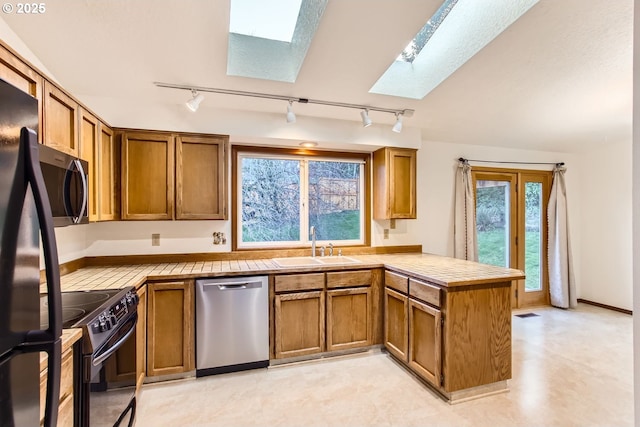 kitchen featuring black appliances, a skylight, kitchen peninsula, tile countertops, and sink