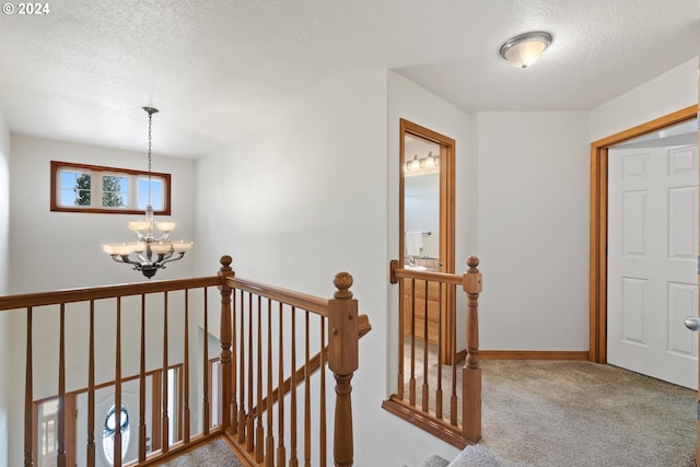 hallway with a textured ceiling, carpet flooring, and an inviting chandelier