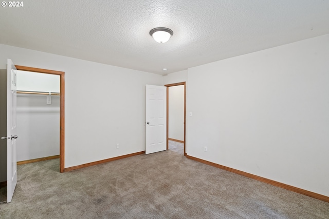 unfurnished bedroom with a closet, light colored carpet, a spacious closet, and a textured ceiling