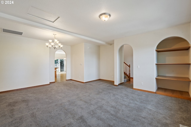 carpeted spare room with built in shelves, a notable chandelier, and a textured ceiling