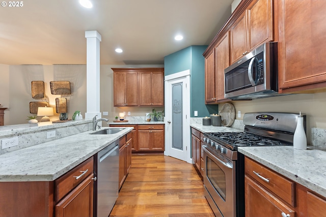 kitchen with light stone counters, sink, stainless steel appliances, and light hardwood / wood-style flooring