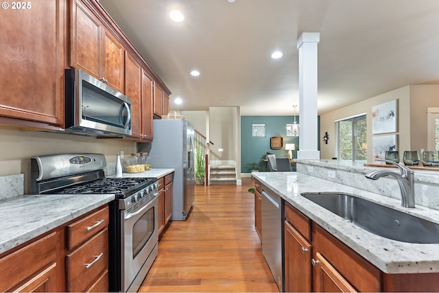 kitchen with sink, light stone countertops, ornate columns, light hardwood / wood-style floors, and stainless steel appliances