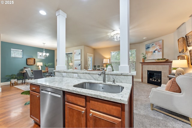 kitchen with light stone countertops, decorative columns, stainless steel dishwasher, sink, and decorative light fixtures