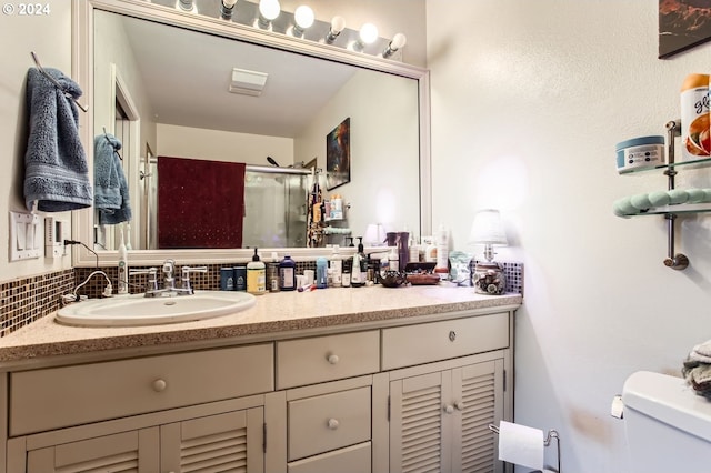 bathroom featuring vanity, toilet, a shower with door, and backsplash