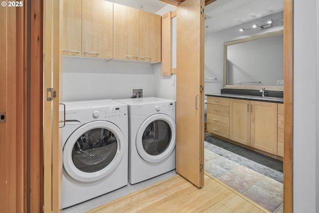 clothes washing area with cabinets, light hardwood / wood-style floors, washer and clothes dryer, and sink